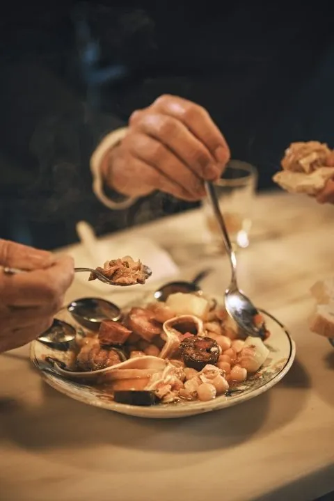 Pessoas a partilhar prato tradicional com colheres à mesa