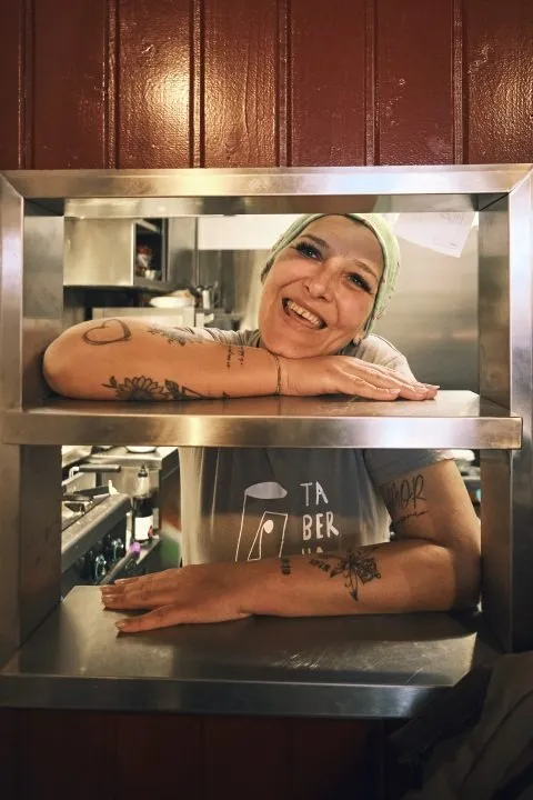 Pessoa da equipa da Taberna do Enteiriço a sorrir na cozinha através da janela de serviço
